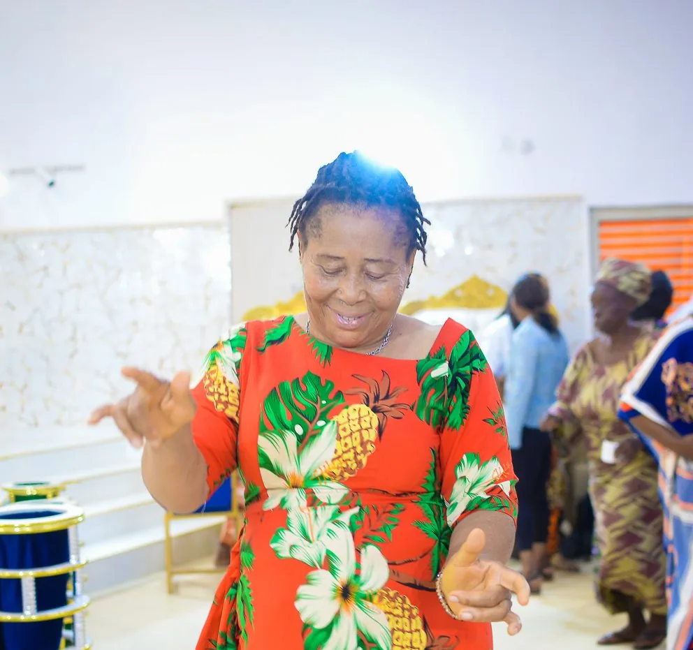 A woman in a bright floral dress dances at the Foundation’s widows’ outreach in Akute.