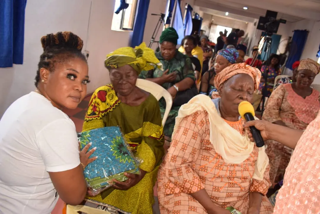 An older woman holding a gift and speaking into a microphone at a Foundation outreach for older mothers.