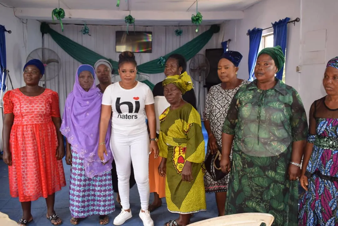 Older women in bright wrappers standing together with Foundation volunteers in a hall.