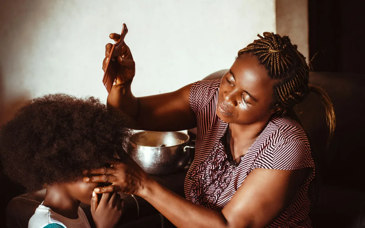 A mother combs her daughter's hair at home in warm afternoon light.